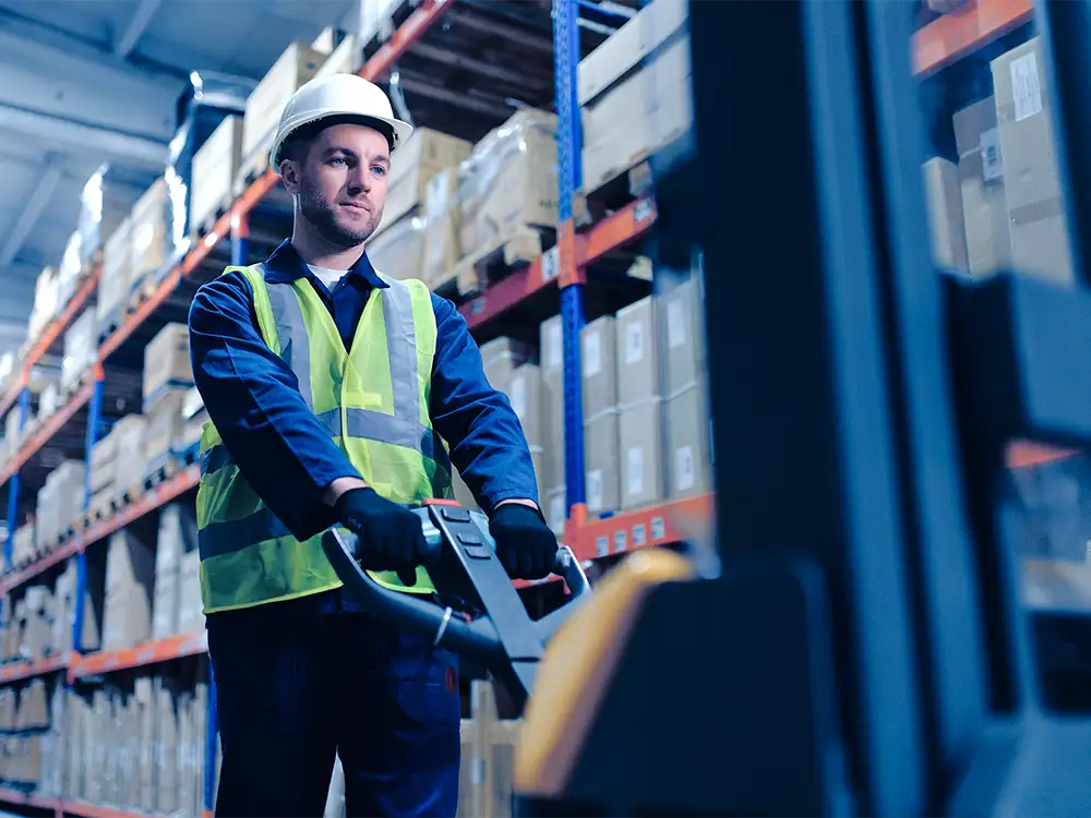 A man pushing a palette down a warehouse aisle.